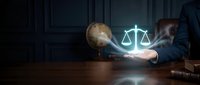 Young male professional in business suit holding glowing scales of justice symbol above wooden desk with globe, representing legal services, law firm expertise, and corporate compliance solutions.