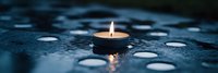 Burning tea light candle on dark blue reflective surface with water drops creating atmospheric panoramic composition. Peaceful meditation background.