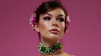 Young Asian woman with glamorous makeup wearing floral accessories and emerald crystal choker necklace against pink background, fashion beauty portrait.