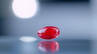 Red transparent pill capsule floating with reflection on smooth surface against blurred background with bokeh light effect.