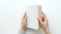 Hands holding open blank notebook with white pages against neutral background, suitable for book cover mockups, publishing, education, and stationery design projects.