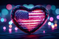 Glowing heart-shaped glass ornament with American flag pattern and sparkling lights against colorful bokeh background for patriotic holidays and celebrations.