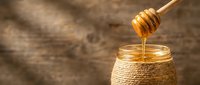 Golden honey dripping from wooden dipper into glass jar on rustic wood background. Natural sweetener for cooking, baking and healthy lifestyle.