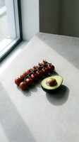 Fresh cherry tomatoes on vine and halved avocado on concrete surface in natural window light, healthy eating concept.