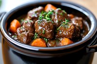 Homemade beef meatballs with carrots and herbs in rich brown gravy sauce, served in black ceramic pot. Traditional comfort food for winter dinner.