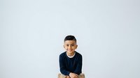 Young boy with dark hair and medium skin tone wearing a navy blue long-sleeved shirt, smiling at camera against white background. Suitable for family, education, and lifestyle marketing materials.