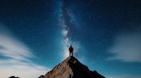 Silhouette of lone hiker standing on mountain peak under starry night sky with bright Milky Way galaxy, clouds and cosmic atmosphere for adventure concepts.