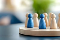 Wooden game pieces on circular board showing blue and natural colored pawns, representing leadership, teamwork and strategic business concepts.