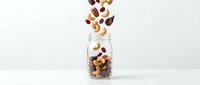 Mixed nuts and dried fruits falling into glass jar on white background, isolated for food packaging, healthy snacking, nutrition advertising, and recipe content.