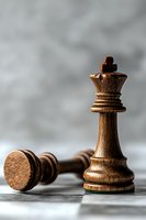 Wooden chess queen piece standing victorious over fallen king on textured surface against blurred gray background, symbolizing strategy and power dynamics.