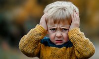 Young boy in yellow knit sweater showing anger and frustration, covering ears with hands against autumn background. Strong emotional expression for childhood behavior concepts.