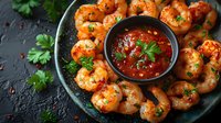 Grilled spicy shrimp served on dark plate with red sauce and fresh herbs. Closeup of seafood appetizer with chili dipping sauce garnished with parsley.