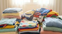Colorful folded clothes and garments organized in neat stacks on bed surface. Laundry sorting and organization concept for household cleaning tasks.