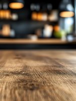 Rustic wooden table surface with natural grain texture in soft focus against dark restaurant interior with warm pendant lighting creates cozy atmosphere.