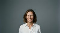 Professional middle-aged Caucasian businesswoman with short brown hair smiling confidently in white shirt against gray studio background for corporate use.