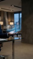 Businessman in dark suit holding holographic financial data display with rising charts and graphs in modern office environment with city skyline view.