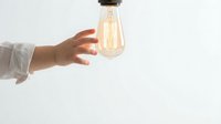 Hand reaching toward glowing vintage Edison bulb against white background symbolizing innovation, creativity and bright ideas for business concepts.