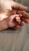 Tiny newborn hand resting in adult palm, close-up macro shot capturing tender parent and baby bond, love, care, and family connection.