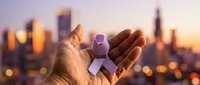 Hands holding purple ribbon awareness symbol against blurred city skyline at sunset, representing health causes, charity support and medical advocacy campaigns.