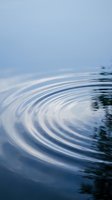 Concentric water ripples creating circular waves on calm blue surface with soft reflections and serene aquatic movement for meditation and wellness concepts.