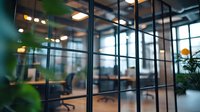 Modern office interior with glass walls and partitions, green plants, and ambient lighting creating professional workspace atmosphere. For corporate and business designs.