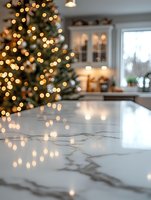 Marble kitchen counter with blurred Christmas tree lights creating magical bokeh effect in modern white kitchen interior during holiday season.