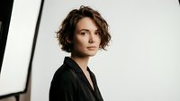 Professional businesswoman with short curly hair in black blazer against modern office background with natural lighting for corporate presentations.