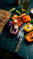 Fresh colorful bell peppers sliced on rustic wooden cutting board with knife, olive oil and spices for healthy cooking and meal preparation.