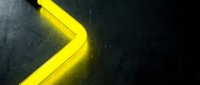 Bright yellow neon arrow glowing on dark textured metal background, pointing right with vivid light effect for modern design projects.