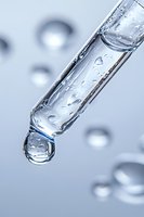 Clear glass pipette with water droplet forming at tip against soft blue background, showcasing liquid surface tension and scientific precision in laboratory setting.