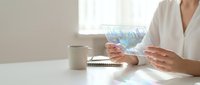 Professional woman in white shirt analyzing holographic data visualization at modern office desk with laptop and coffee cup for business analytics.