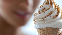 Creamy soft serve ice cream swirled in waffle cone decorated with golden sprinkles against blurred background. Sweet summer dessert close-up.