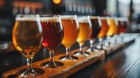 Craft beer tasting flight with various amber and golden ales arranged on wooden board in modern brewery taproom for sampling experience.