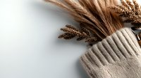 Cozy autumn composition with dried sorghum stems and knitted beige sweater on light background, creating warm minimalist seasonal mood.
