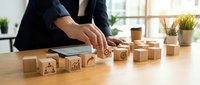 Business professional arranging wooden blocks with startup icons on desk in modern office workspace for entrepreneurship and innovation concepts.
