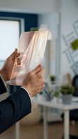 Male professional in dark business suit holding transparent glass panel with light refraction in modern office environment.