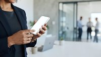 Businesswoman holding smartphone in modern office environment with colleagues in background, suitable for corporate technology and business communication concepts.