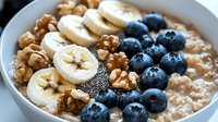 Healthy breakfast bowl with oatmeal porridge topped with fresh blueberries, sliced banana, chia seeds and crunchy walnuts, close up view of morning meal.