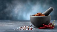 Stone mortar with crushed red chili peppers and spices on blue background, showcasing traditional cooking ingredients for spicy cuisine preparation.