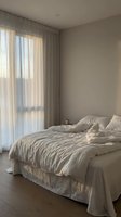 Minimalist bedroom interior with unmade bed, soft natural lighting through sheer curtains, neutral beige tones creating cozy morning atmosphere for home decor.