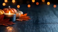 Autumn candle glowing warmly with orange pumpkins and fall leaves on dark wooden surface, creating cozy seasonal atmosphere with bokeh lights.
