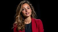 Young Hispanic businesswoman with wavy brown hair wearing red blazer and black top smiling confidently against dark background, professional corporate portrait.