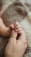 Tender moment of parent holding newborn baby hand with wedding ring on cozy knit blanket background showing love, family bond and new life beginning.