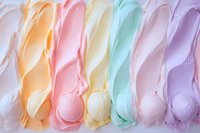 Colorful pastel meringue swirls in soft rainbow shades of orange, pink, yellow, mint and purple arranged in rows creating sweet textured background pattern.