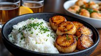 Pan-seared caramelized sea scallops served with steamed white rice garnished with fresh chopped herbs, accompanied by golden-brown seafood in savory sauce.