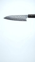 Damascus steel chef knife with dark handle featuring distinctive wavy pattern on blade, isolated on white background for culinary and kitchen tool applications.