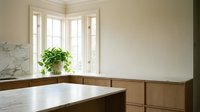 Luxury bathroom corner with marble countertop, wooden cabinetry, potted green plant on windowsill, and bright natural light from French doors.