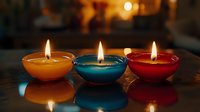 Colorful aromatic candles in glass bowls with burning flames reflecting on dark glossy surface against warm blurred background create cozy atmosphere.