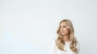 Young woman with long blonde wavy hair wearing white shirt against neutral background, suitable for corporate, lifestyle, and beauty marketing materials.