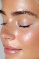 Close up of young woman's face with natural freckles, closed eyes, long eyelashes and glowing dewy skin showing minimal makeup beauty look for cosmetic advertising.